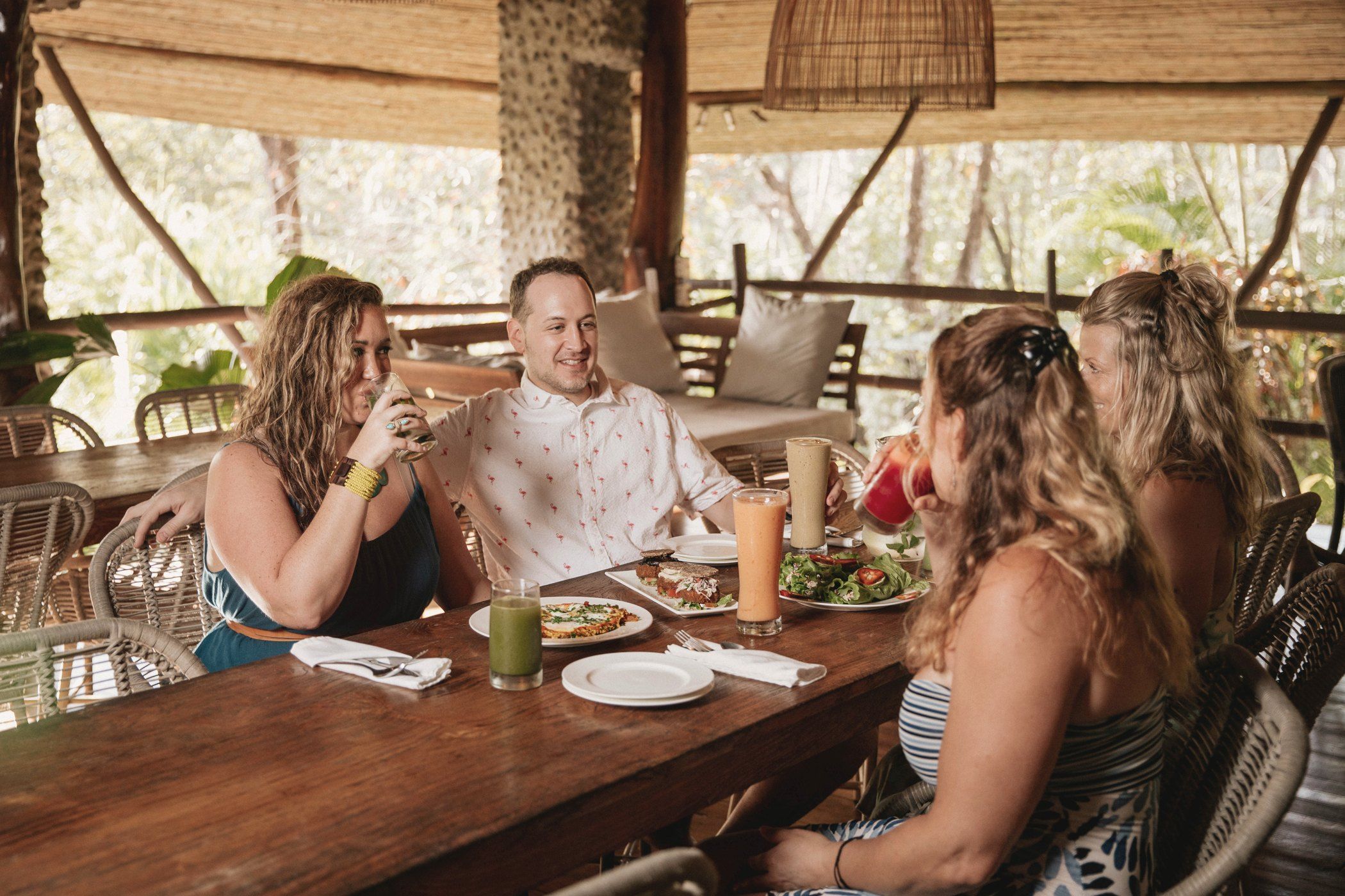 Guests share a colourful, fresh meal together at a long wooden table under the palapa